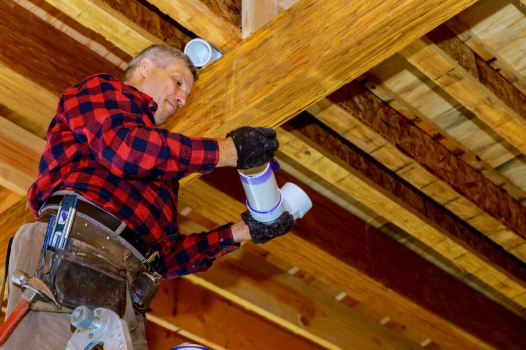 Roofer sealing a vent pipe in an attic to help prevent condensation